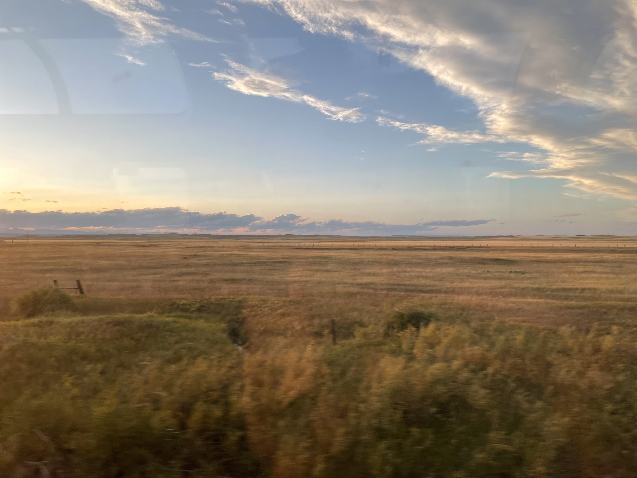 Open plains at dusk under a wide sky, seen from a train window.